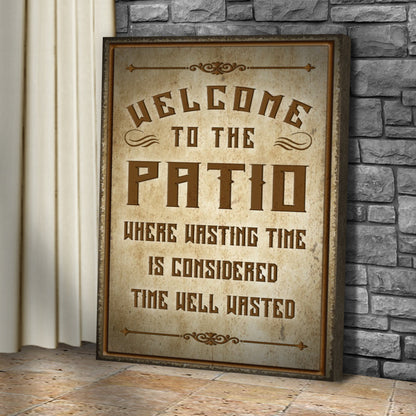 Tall Welcome To The Patio canvas sign in tan leaning against a gray stone wall beside a curtain