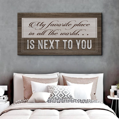 My Favorite Place in All the World Is Next to You canvas sign in taupe with a dark wood-look border, above a bed