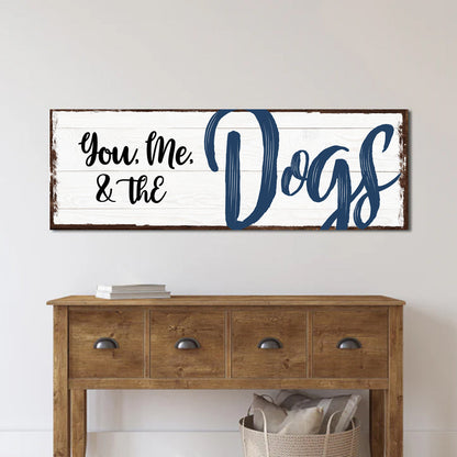 White plank-look canvas sign with dark edges reading You, Me, & the Dogs, with Dogs in navy brush script, above a console