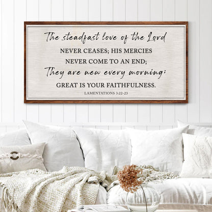 Canvas sign with the Lamentations 3:22-23 verse in dark script and capitals on cream with a brown border, above a white sofa