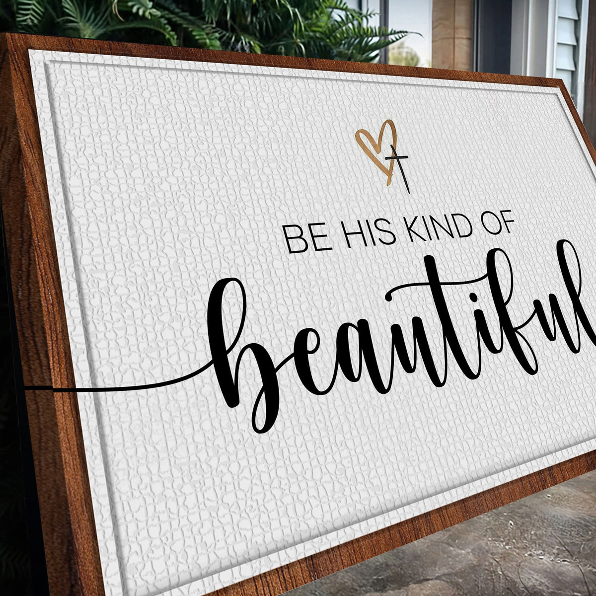 White canvas sign with a gold heart and cross and black script reading Be His Kind of Beautiful, seen at an angle
