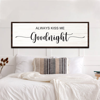 Always Kiss Me Goodnight canvas sign in the clean dark border style, hung above a white bed with a striped pillow