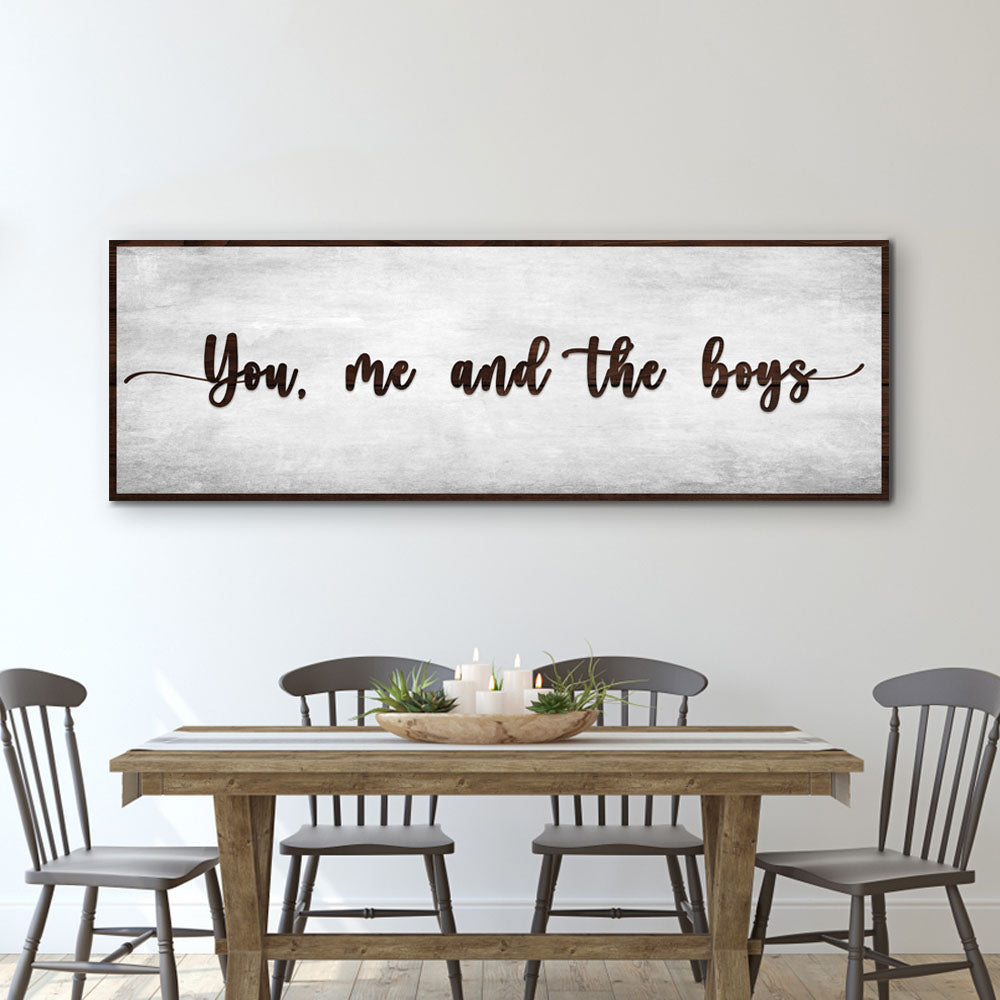 Wide canvas sign with a weathered gray look and brown script reading You, me and the boys, above a dining table
