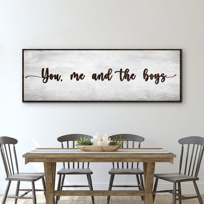 Wide canvas sign with a weathered gray look and brown script reading You, me and the boys, above a dining table