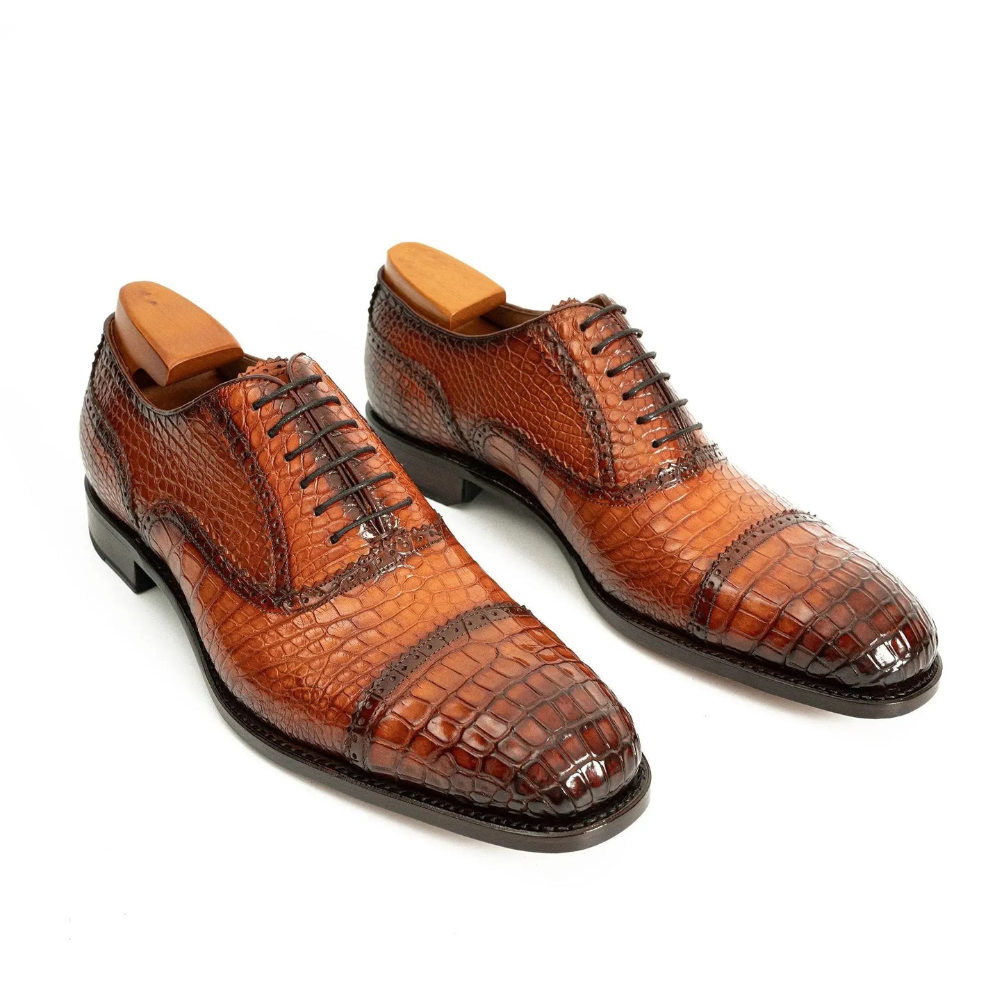 Pair of brown leather dress shoes with crocodile textured design on a white background