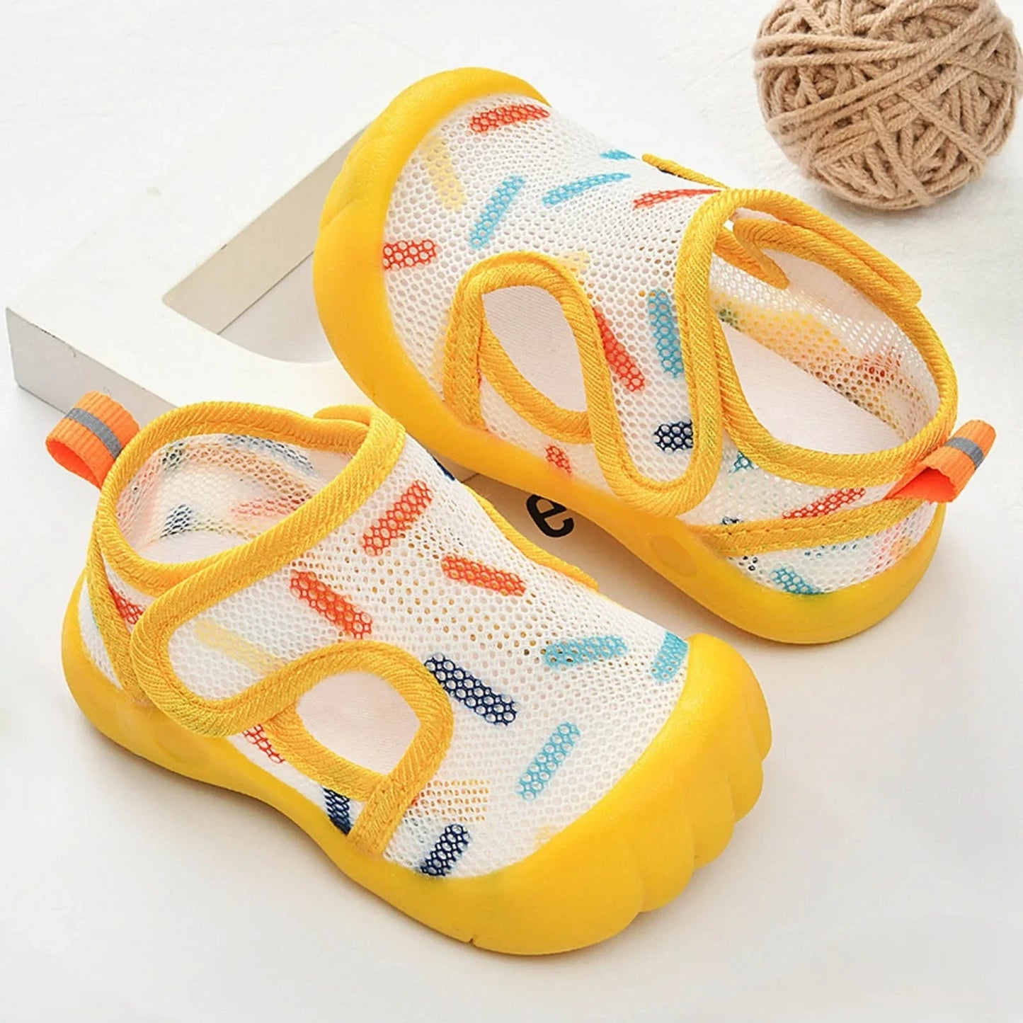 Pair of yellow baby water shoes with heart stripes on a white background