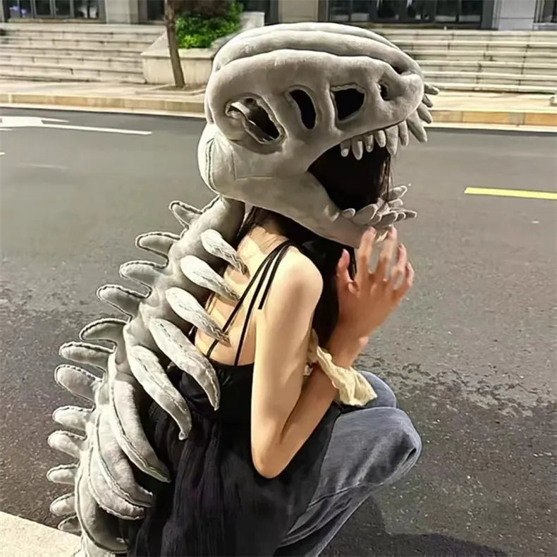 Person wearing a large, gray, dino-like creature headpiece on an urban street.