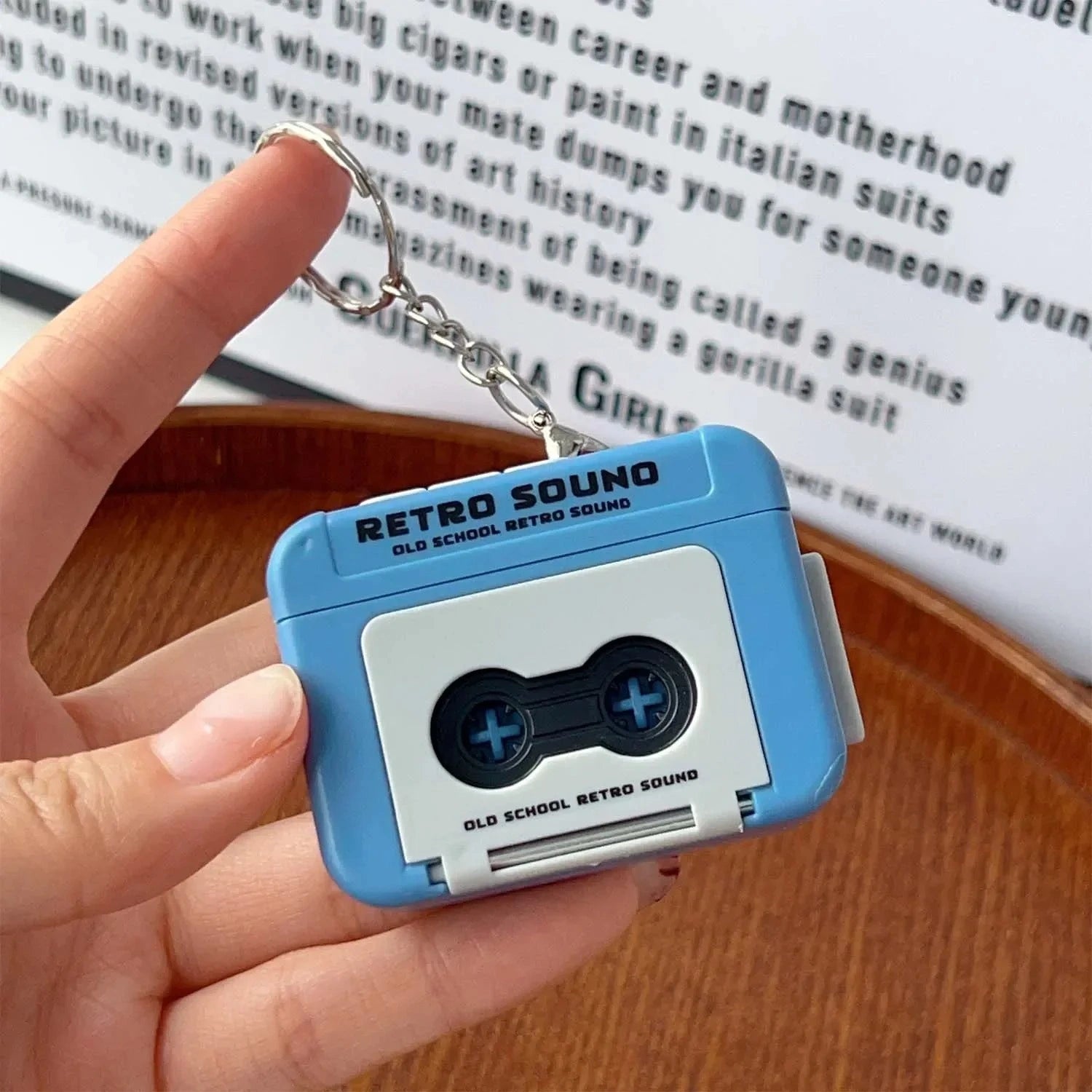 Retro cassette blue tape keychain held by a hand with a book in the background