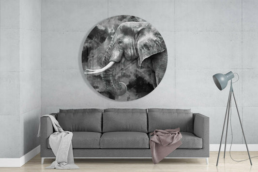 Black and white elephant profile round glass wall art above a gray sofa beside a tripod floor lamp on a pale concrete wall