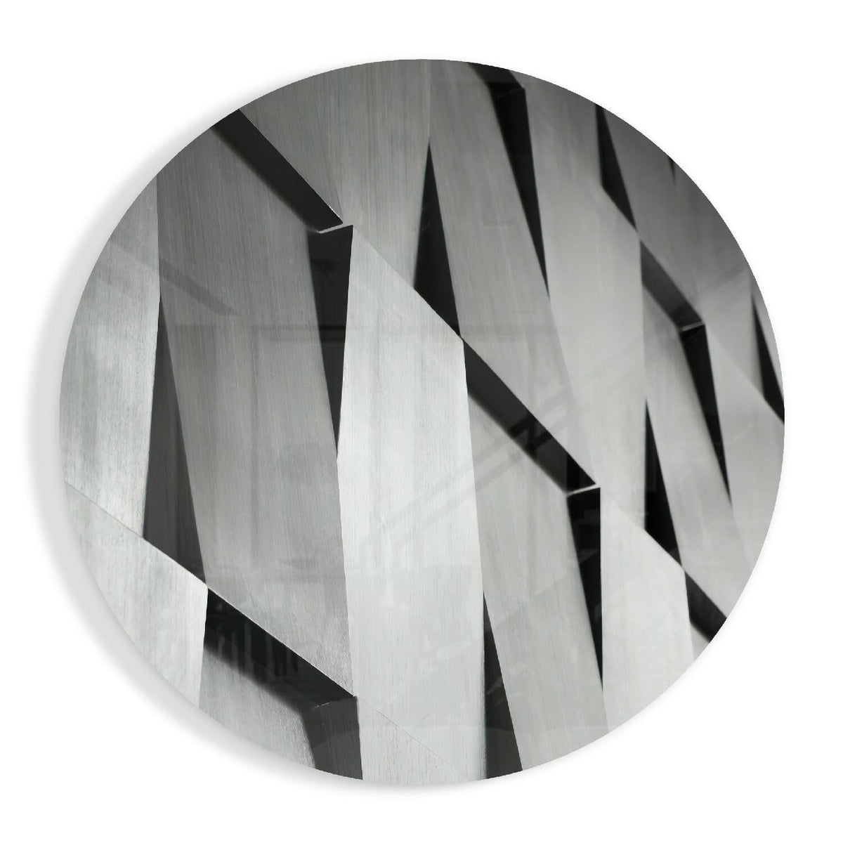 Round glass disc with angled silver gray slats and sharp black shadows in a geometric pattern