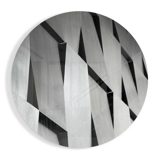 Round glass disc with angled silver gray slats and sharp black shadows in a geometric pattern