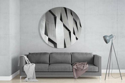 Silver geometric slats round glass wall art above a gray sofa beside a gray tripod floor lamp on a pale concrete wall