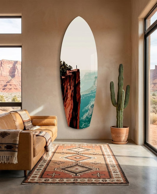 Red canyon surfboard glass wall art in a desert-view room with a tan leather sofa, a potted cactus and a patterned rug