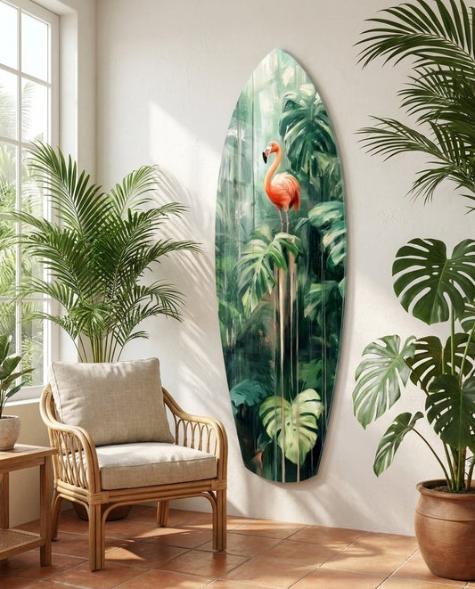 Jungle flamingo surfboard glass wall art on a white wall beside a rattan armchair and potted palms