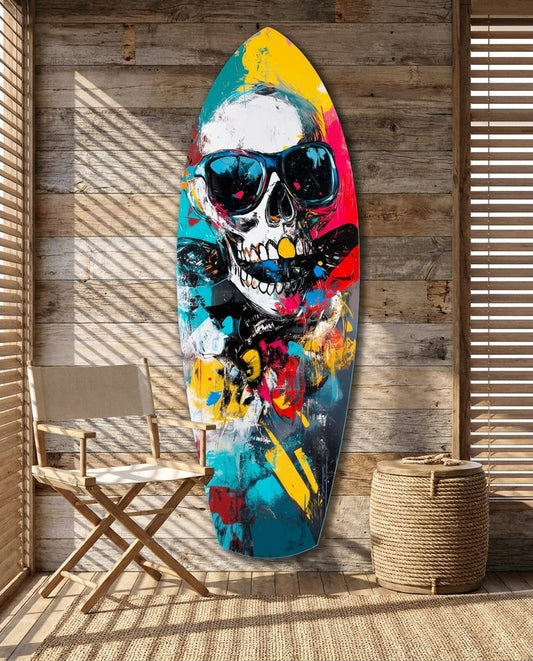 Grinning skull in blue sunglasses with teal, yellow and red paint splatter on surfboard glass art by a wood wall