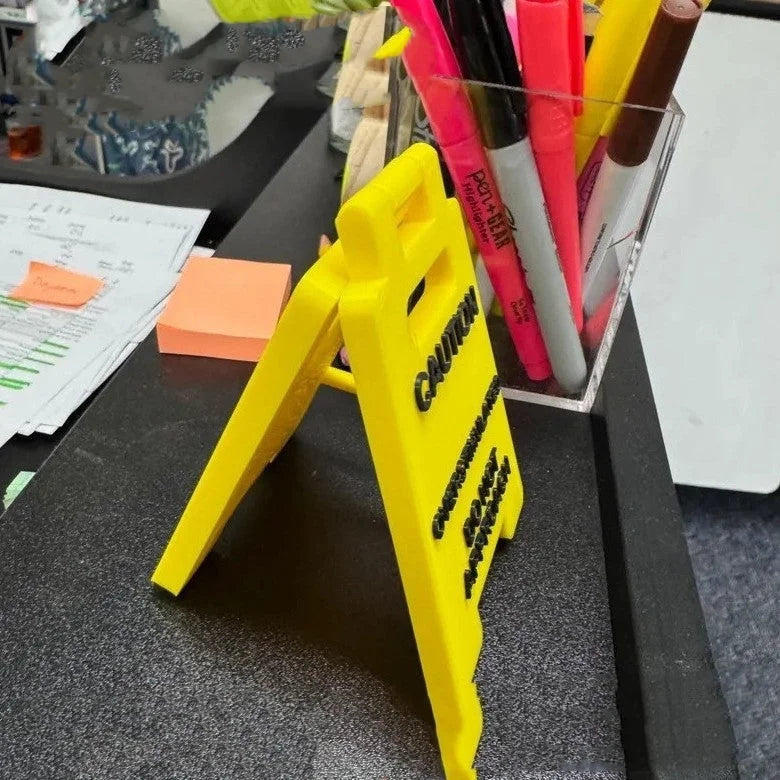 Side angle of the mini caution sign standing on a cluttered office desk.