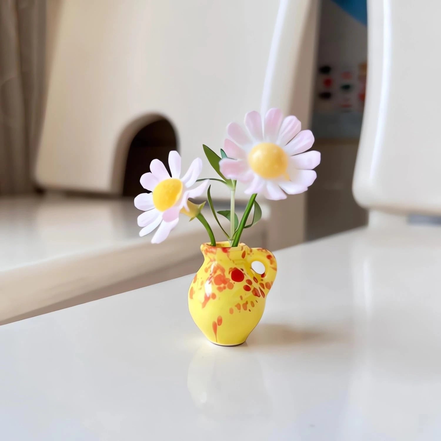 Small yellow vase with floral design containing pink and yellow flowers on a white surface.