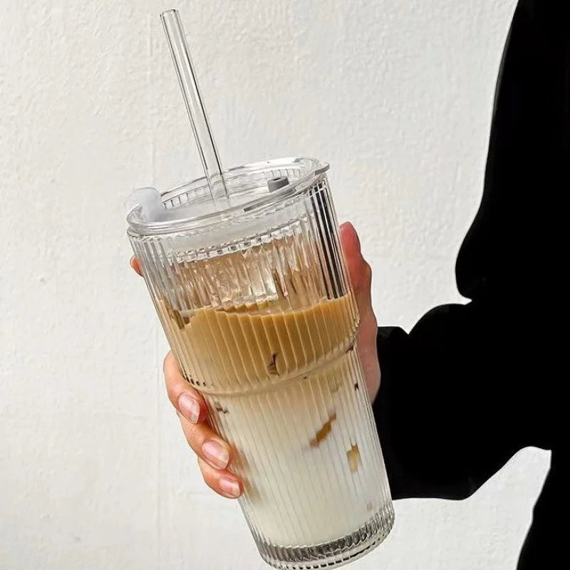 Striped glass cup with lid and straw filled with iced coffee and milk layers

