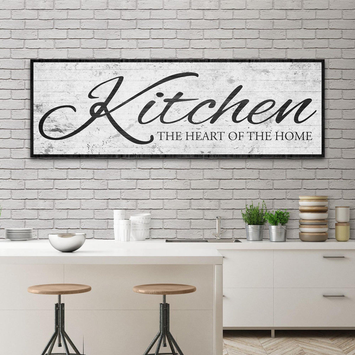 White distressed canvas sign with the word Kitchen in black script and a black border above a kitchen island with stools