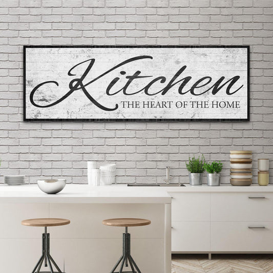 White distressed canvas sign with the word Kitchen in black script and a black border above a kitchen island with stools