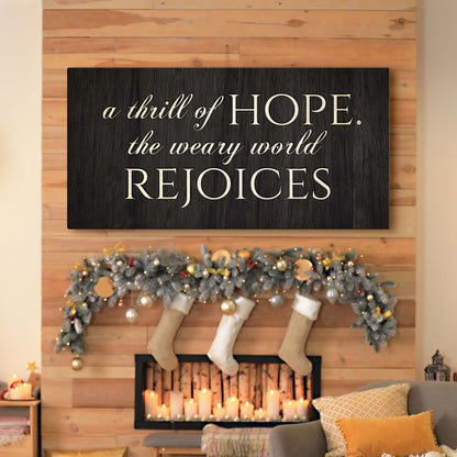 Wide black wood-look canvas sign with a cream Christmas hymn line, hung over a fireplace with stockings and garland