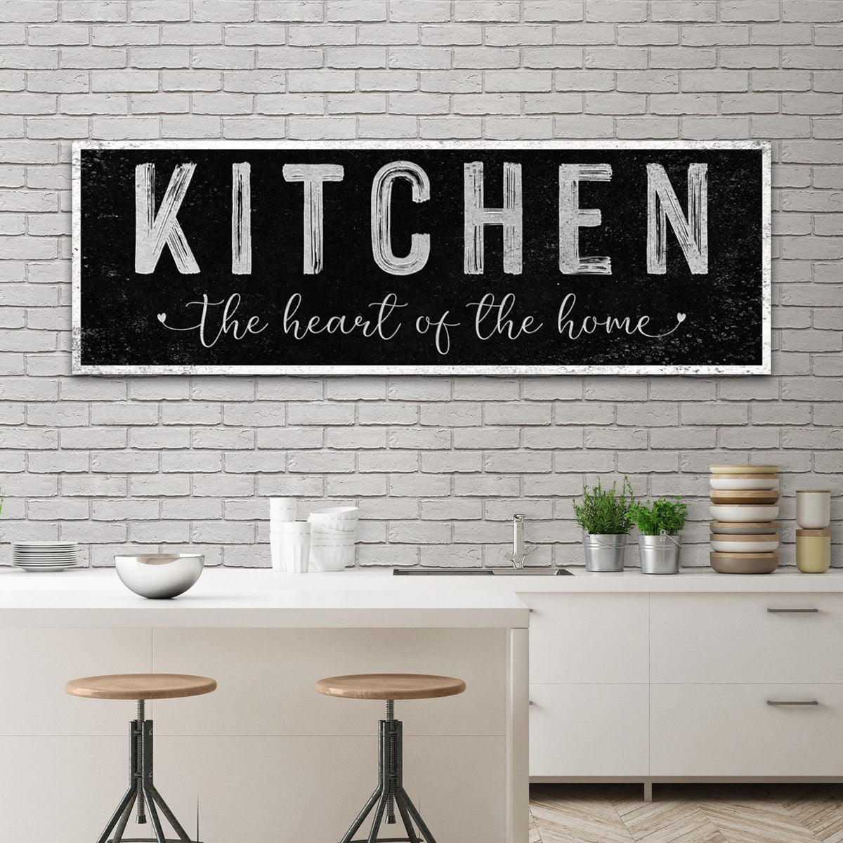 Black distressed canvas sign with Kitchen in white block capitals and a script line, above a kitchen island with stools
