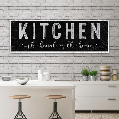 Black distressed canvas sign with Kitchen in white block capitals and a script line, above a kitchen island with stools