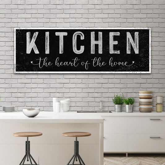 Black distressed canvas sign with Kitchen in white block capitals and a script line, above a kitchen island with stools