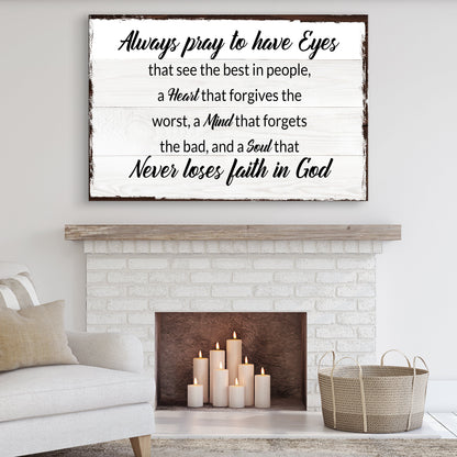 White wood-look canvas sign with a dark edge and black lettering that begins Always pray to have Eyes, above a fireplace