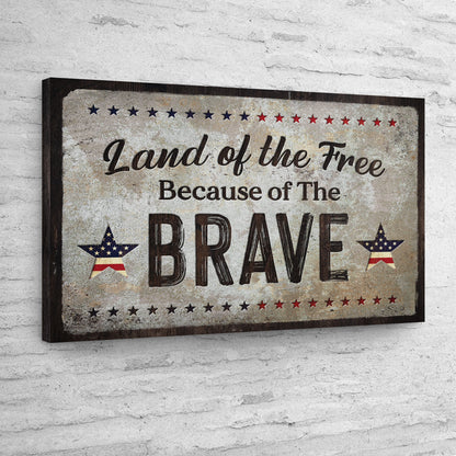 Angled view of the Land of the Free gray patriotic canvas sign on a white brick wall