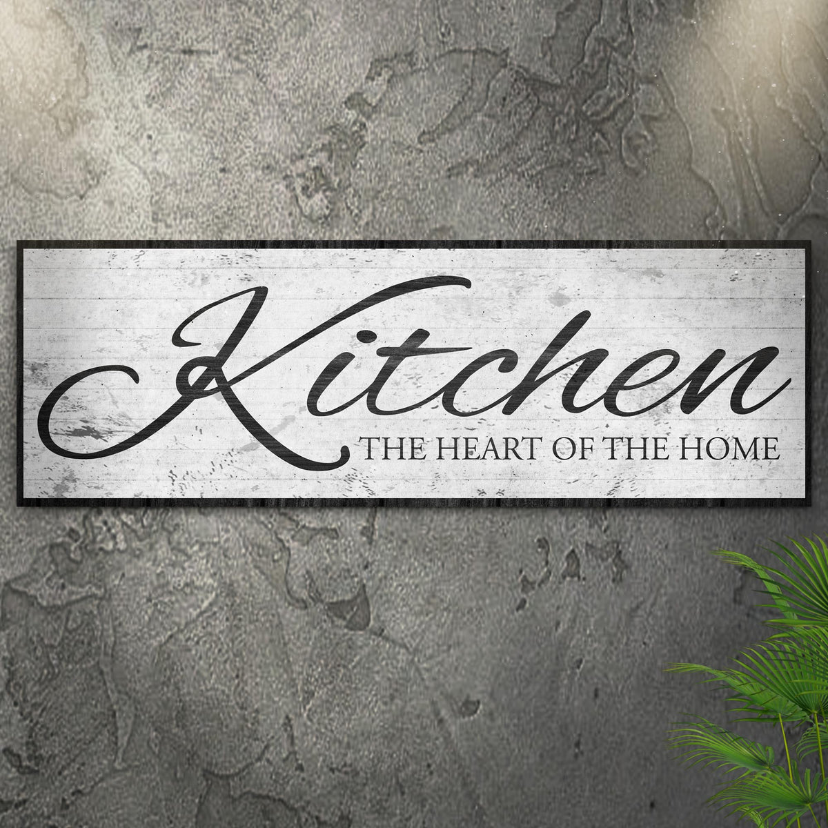 Kitchen Heart of the Home White Script canvas seen at an angle on a gray concrete wall with leaves, view 2