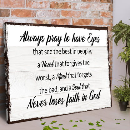 Angled view of the Always Pray to Have Eyes canvas sign leaning against a red brick wall