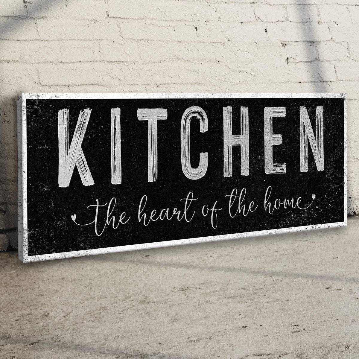 Kitchen Heart of the Home Black canvas seen at an angle on a brick wall above a wood floor, view 3