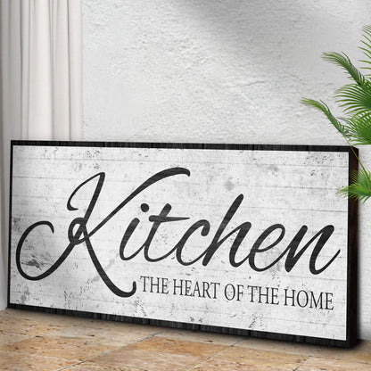 Kitchen Heart of the Home White Script canvas seen at an angle on a concrete wall above a wood floor, view 3