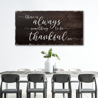 Thankful script canvas sign in the dark wood-look style with white lettering above a dining table with black chairs
