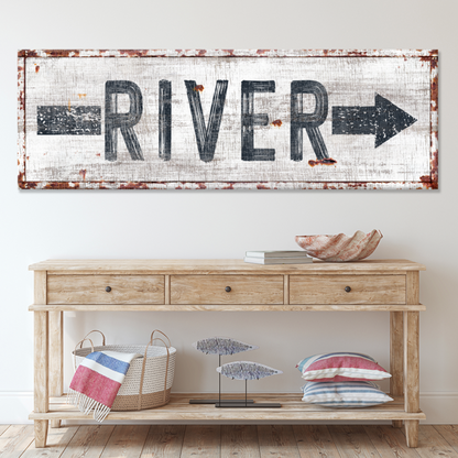 River arrow canvas sign in gray letters on weathered white, above a wood console table