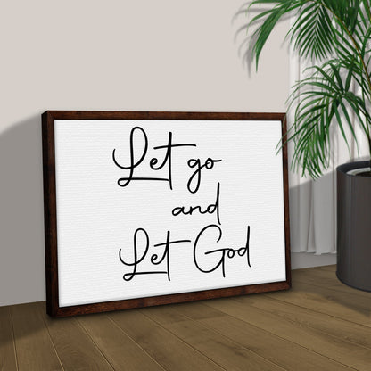 Let Go and Let God Fine Script canvas leaning on a tan wall on a wood floor beside a palm, angled view
