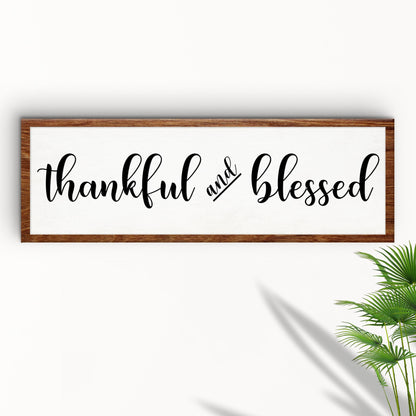 Thankful and Blessed Wood-Look Border canvas on a white wall beside a palm leaf, angled view