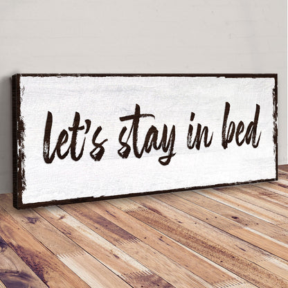 Angled view of the Let's Stay in Bed brush script canvas sign leaning on a wood floor
