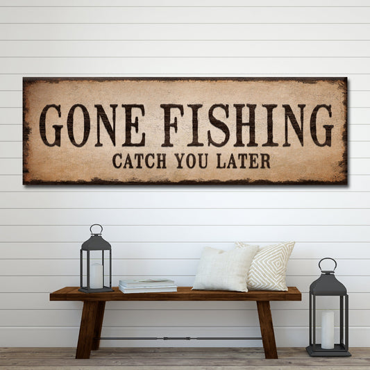 Long tan canvas sign with dark block letters reading Gone Fishing, Catch You Later, above a wood bench with lanterns