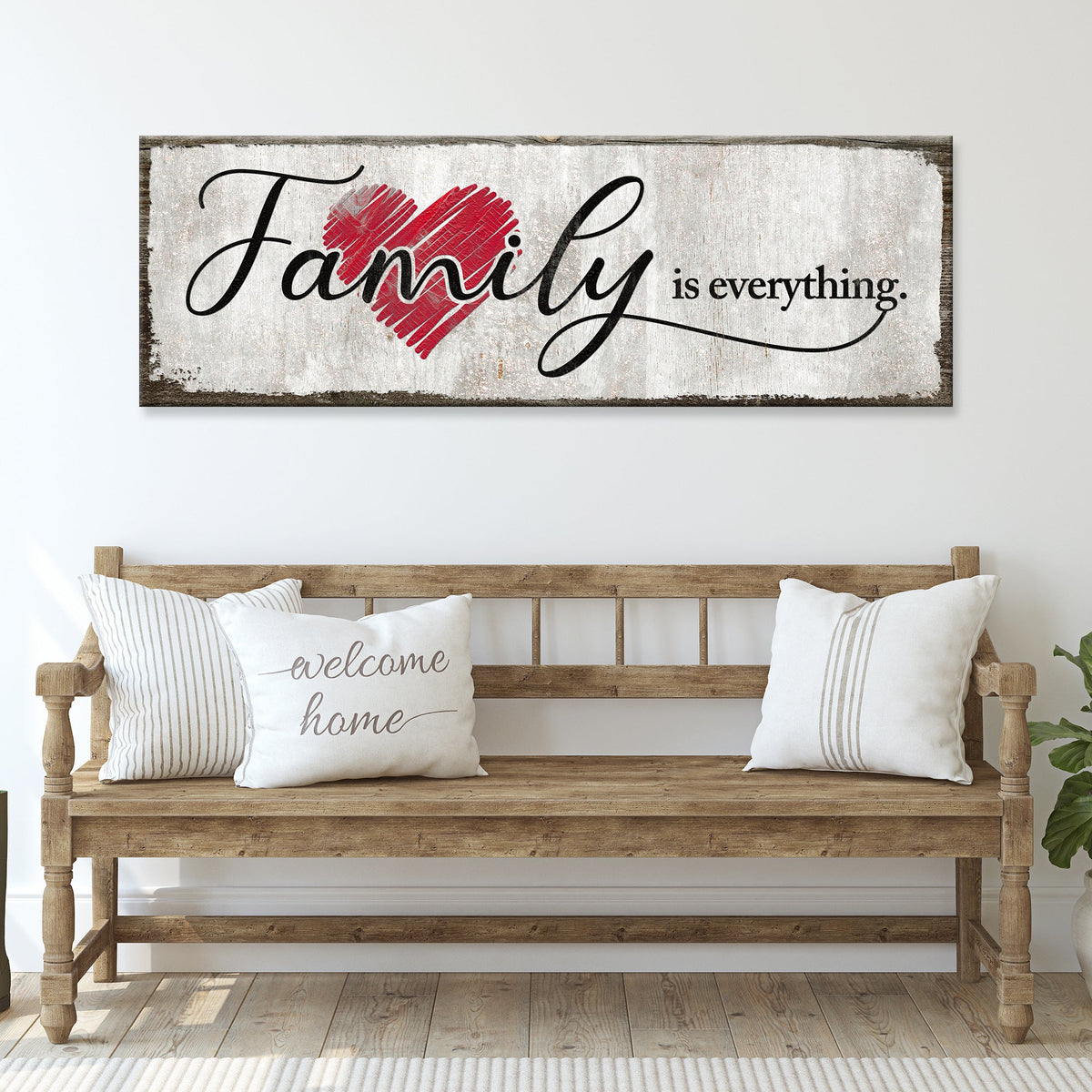 Family Is Everything canvas sign with black script over a red heart, above a wooden bench with white pillows