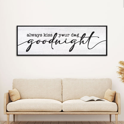 Wide white canvas sign reading always kiss your dog goodnight in black script with paw prints, above a cream sofa