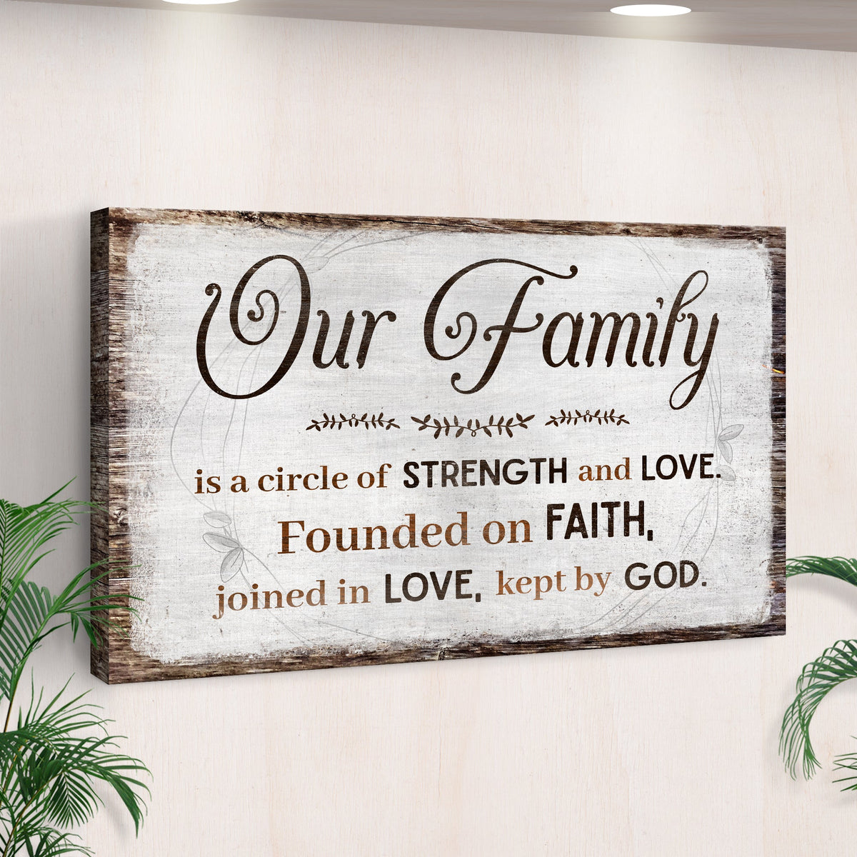 Our Family canvas sign with a saying about strength, love and faith on rustic white, seen at an angle by a palm