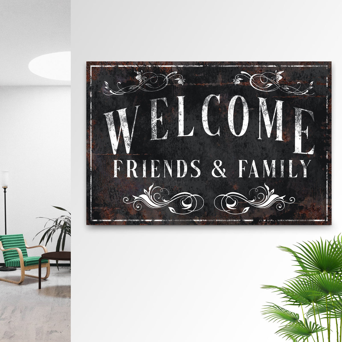 Black distressed Welcome Friends and Family canvas sign with white scrollwork on a white wall beside palm leaves
