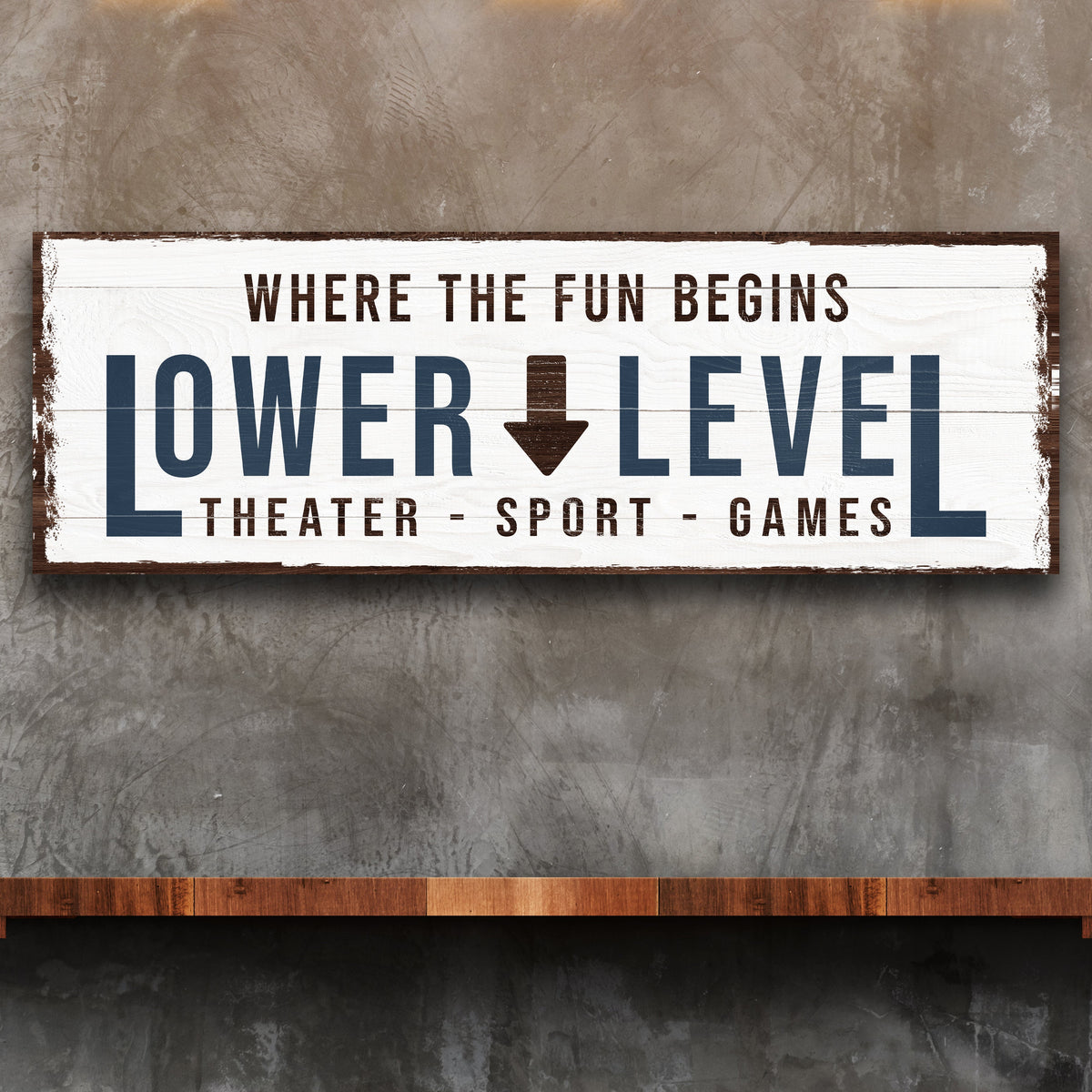 White plank-look canvas sign reading Lower Level with a brown down arrow, on a gray concrete wall above a wood shelf