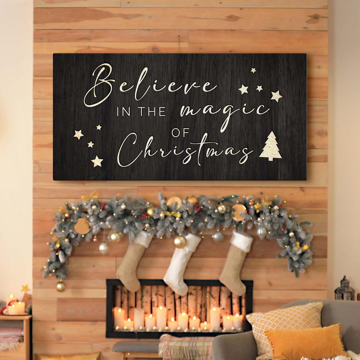 Black canvas sign with cream script reading Believe in the Magic of Christmas above a mantel with stockings and garland