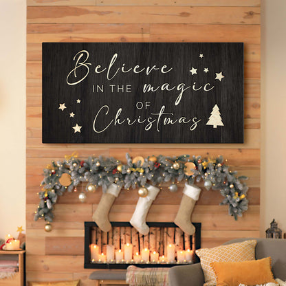 Black canvas sign with cream script reading Believe in the Magic of Christmas above a mantel with stockings and garland