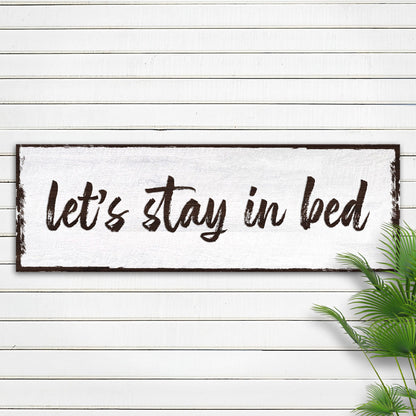 Let's Stay in Bed brush script canvas sign on white shiplap beside a palm leaf