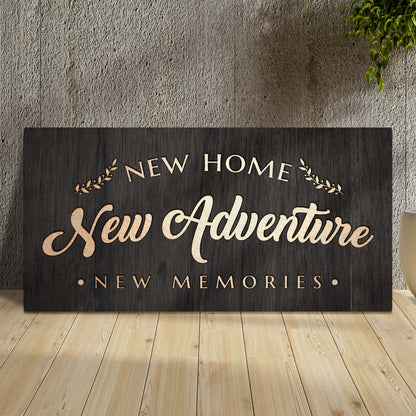 New Home New Adventure dark wood-look canvas leaning against a concrete wall on a light wood floor