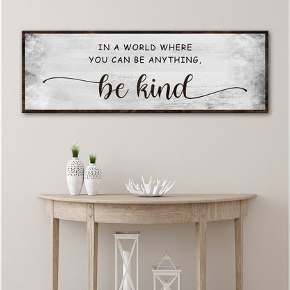 Be Kind soft gray canvas sign above a half-round wood console table with white vases